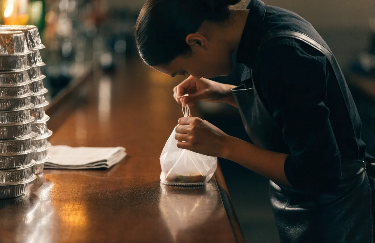 A sealed takeout bag standing on a bare counter with condensation beneath it after service